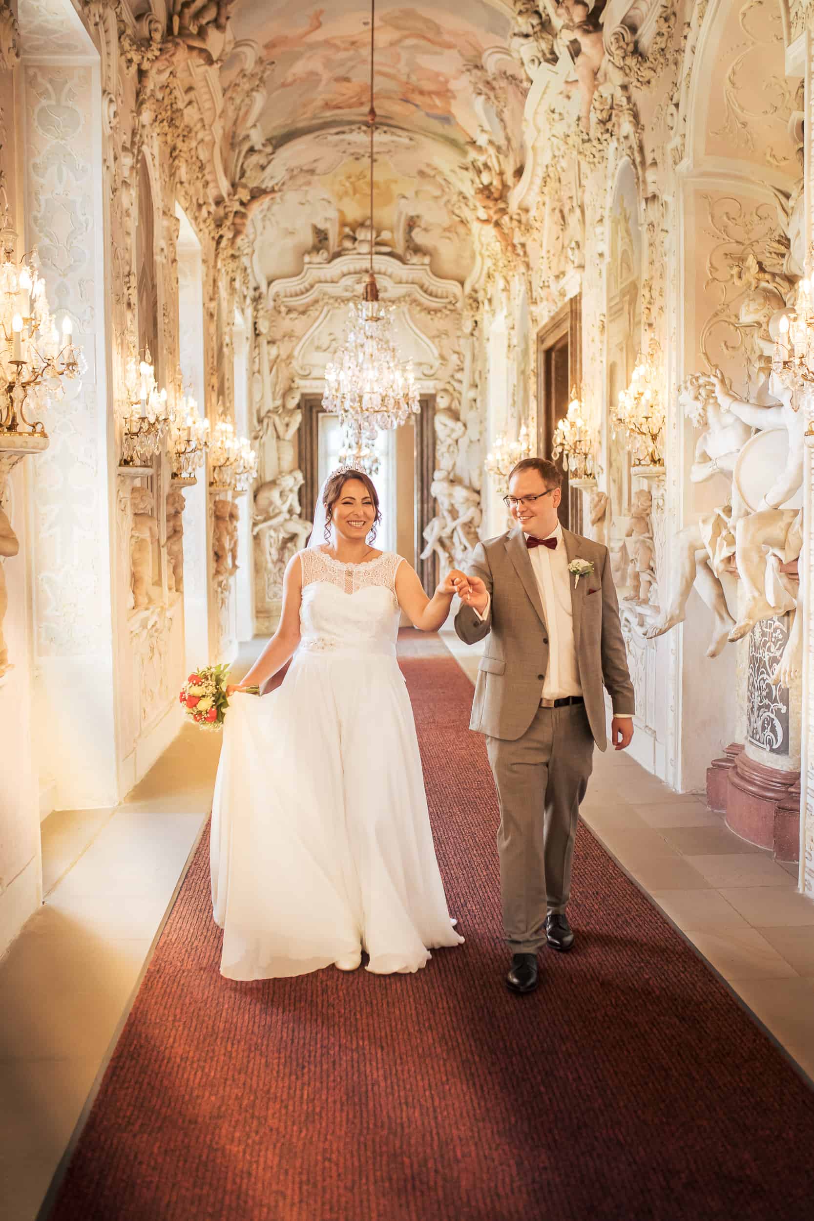 Hochzeitsfotograf Ludwigsburg – Brautpaar im prunkvollen Schlossflur mit Kronleuchtern.