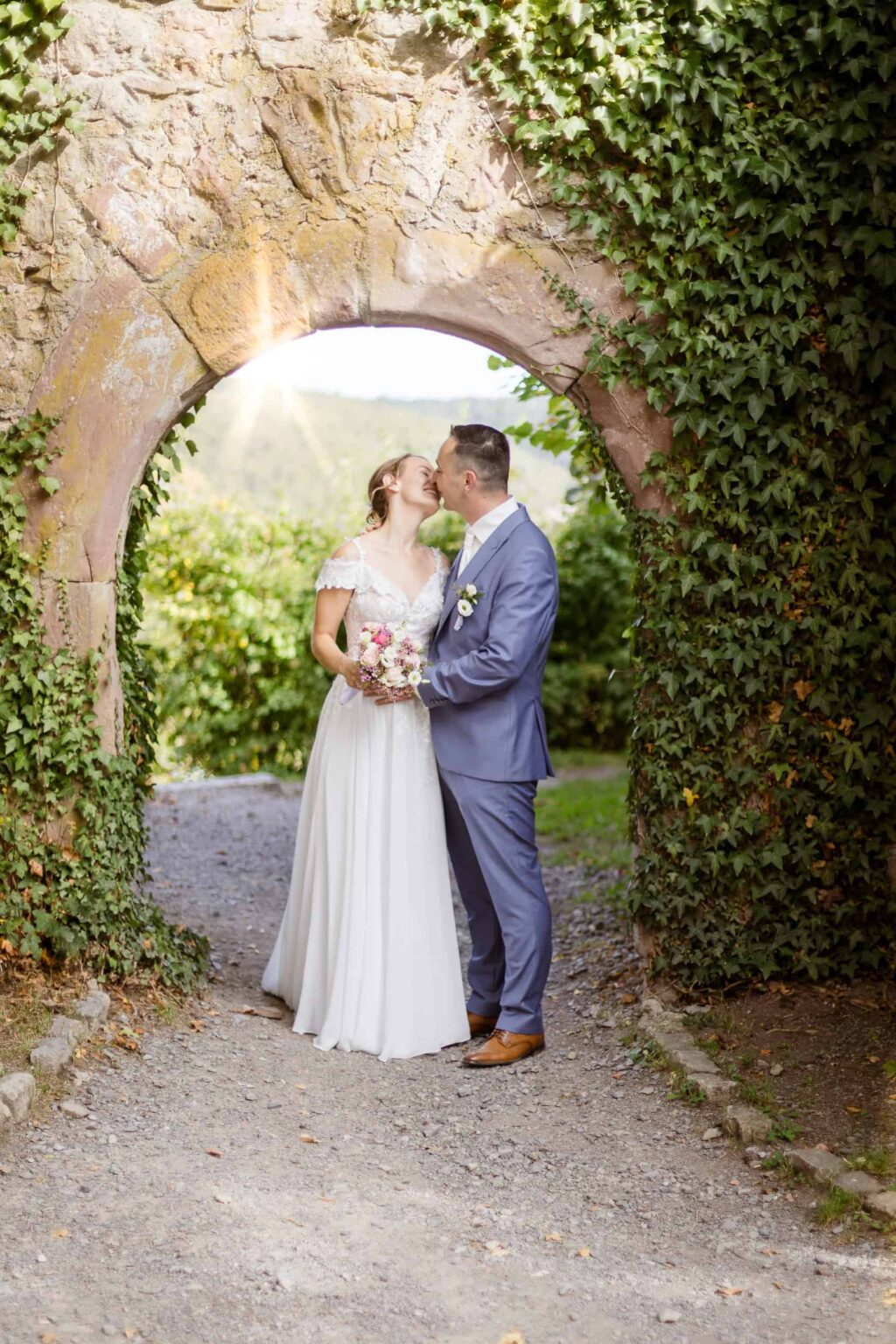 Hochzeitspaar Lisa und Max vor einem alten Steinbogen in Nagold, umgeben von Natur.