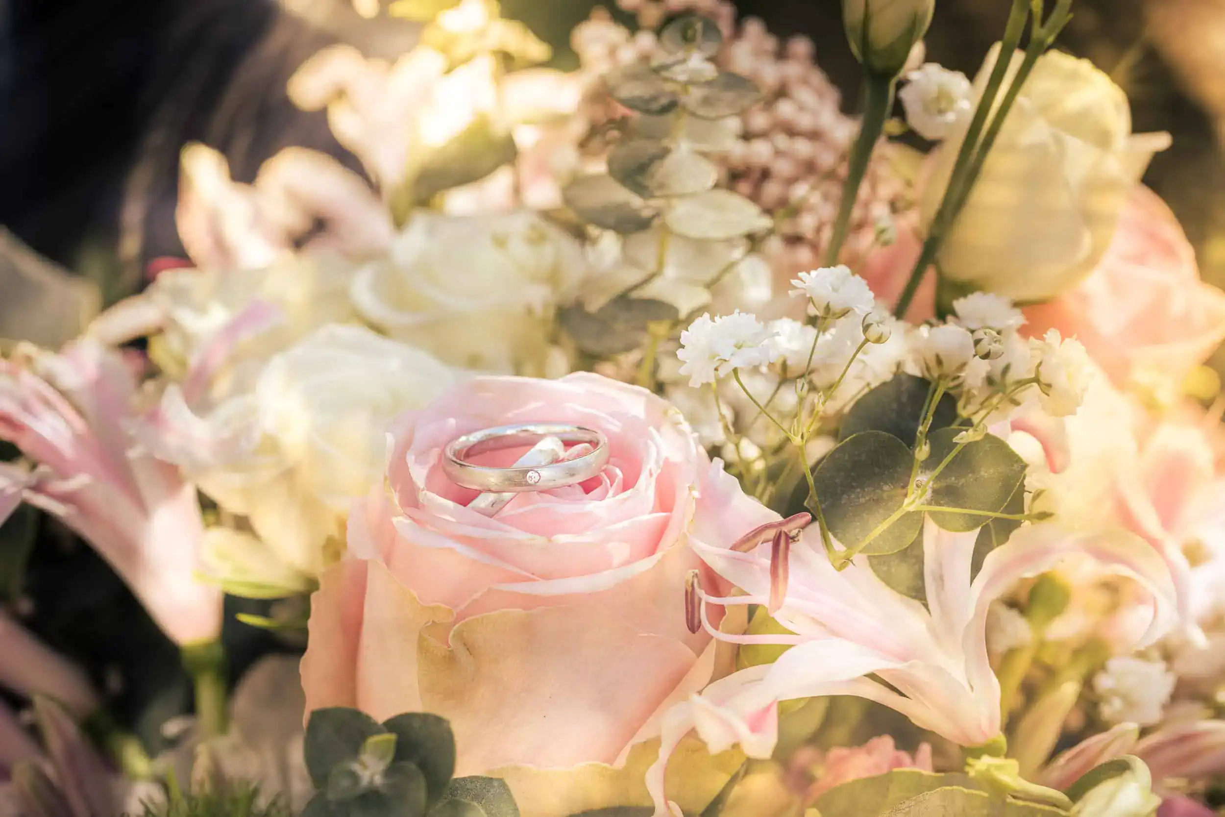 Eheringe auf rosa Rose im Hochzeitsstrauß in sanftem Licht
