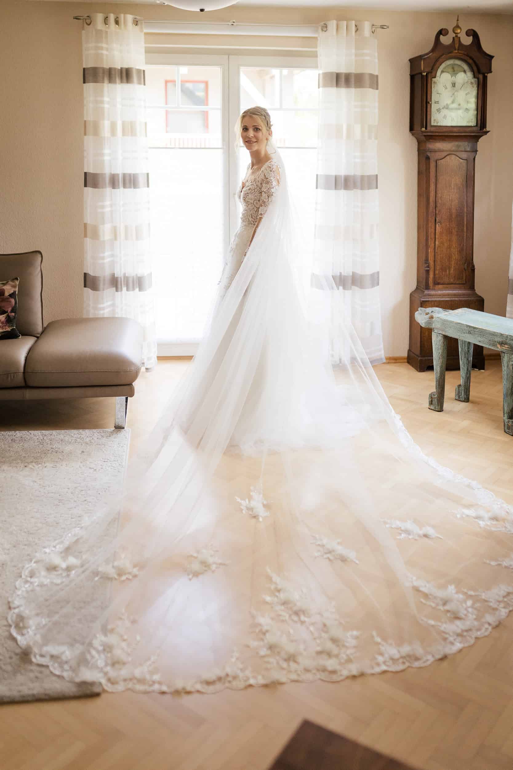 Braut mit langem Schleier steht lächelnd im Zimmer vor der Hochzeit