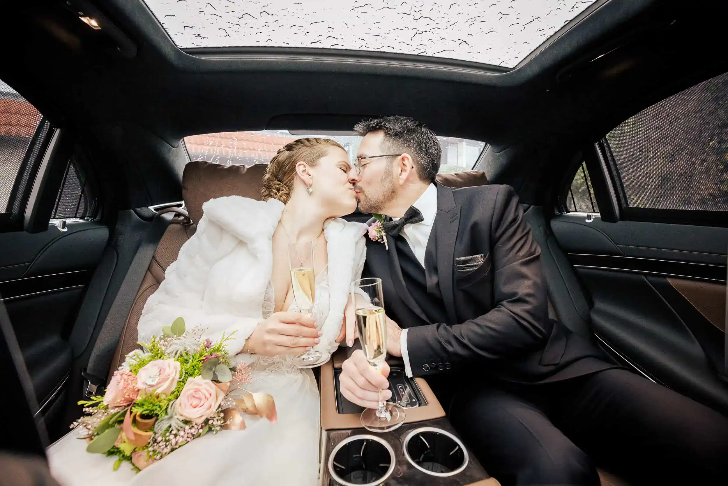Brautpaar küsst sich im Hochzeitsauto mit Sektgläsern – elegante Feier