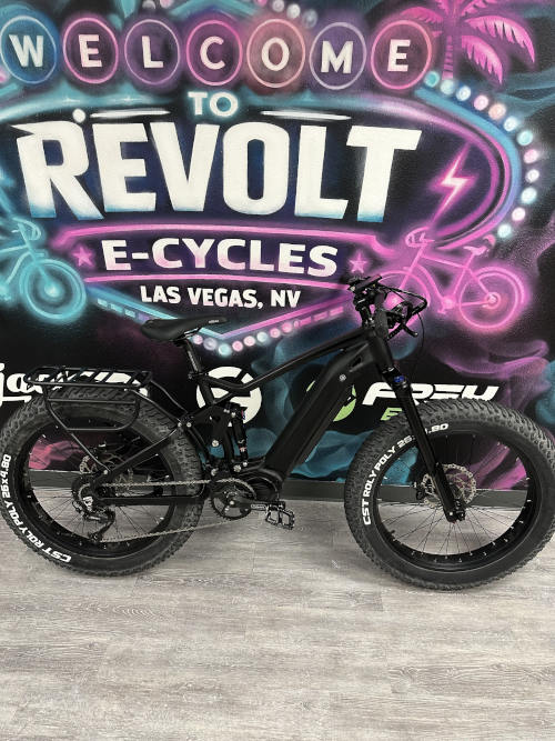 Black JP Fat Black electric fat bike with fat tires and a rear rack, against a neon "Revolt E-Cycles" sign.