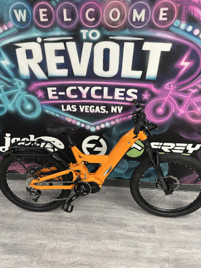Custom CC Ultra Orange Bright orange electric bike parked in front of a neon "Revolt E-Cycles Las Vegas" mural.