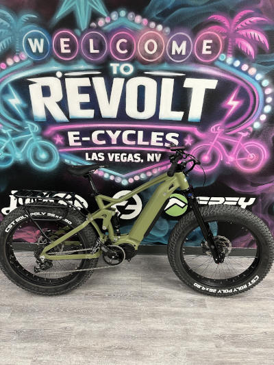 Green jp fat Olive green electric fat tire bike against a neon "Revolt E-Cycles Las Vegas" sign.