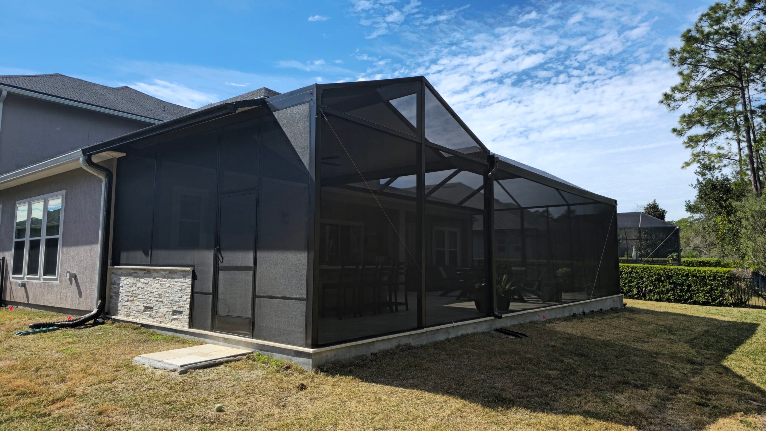 A modern patio with custom screen enclosures Jacksonville, featuring a spacious seating area and lush greenery in the backgro