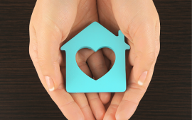 person handing out a home with a heart carved on it
