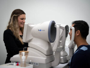 Are Annual Eye Exams Worth It? How Often You Really Need an Eye Test 1 Smiling woman performs eye exam on man using advanced ophthalmic equipment.