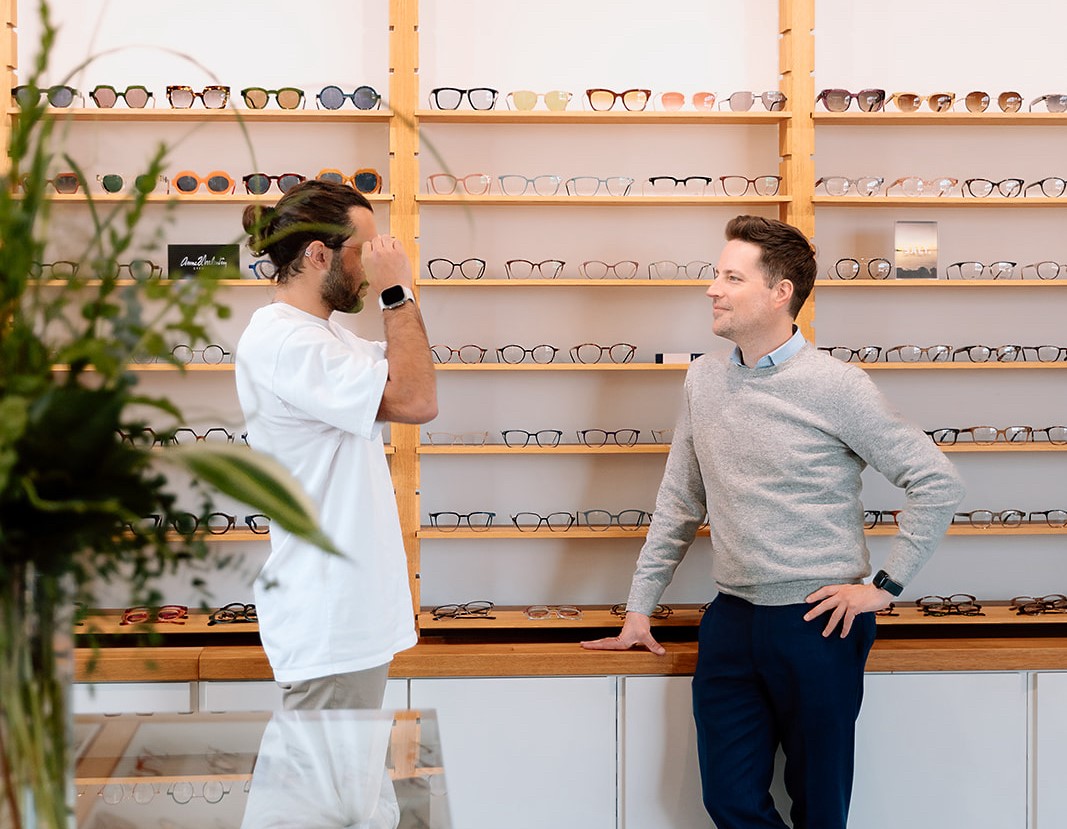 SPECTACLE - Modern Vision Care + Optical Customer tries glasses with help from a sales associate in a bright optical store.