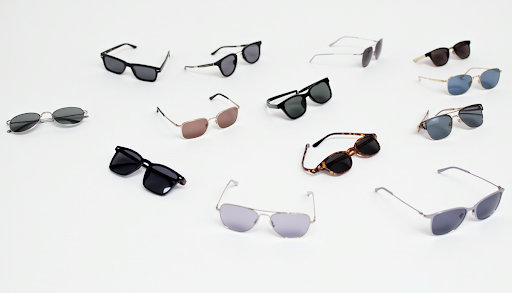 SPECTACLE - Modern Vision Care + Optical A diverse collection of trendy sunglasses displayed on a white background, featuring aviator, square, wire-frame, and tortoise shell styles.