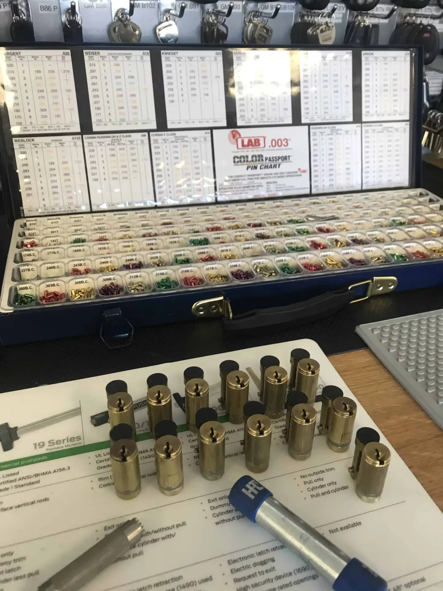 4 Reasons to Rekey Your Locks A professional locksmith rekeying kit featuring a case of color-coded key pins alongside multiple brass lock cylinders and a plug follower tool on a workbench.