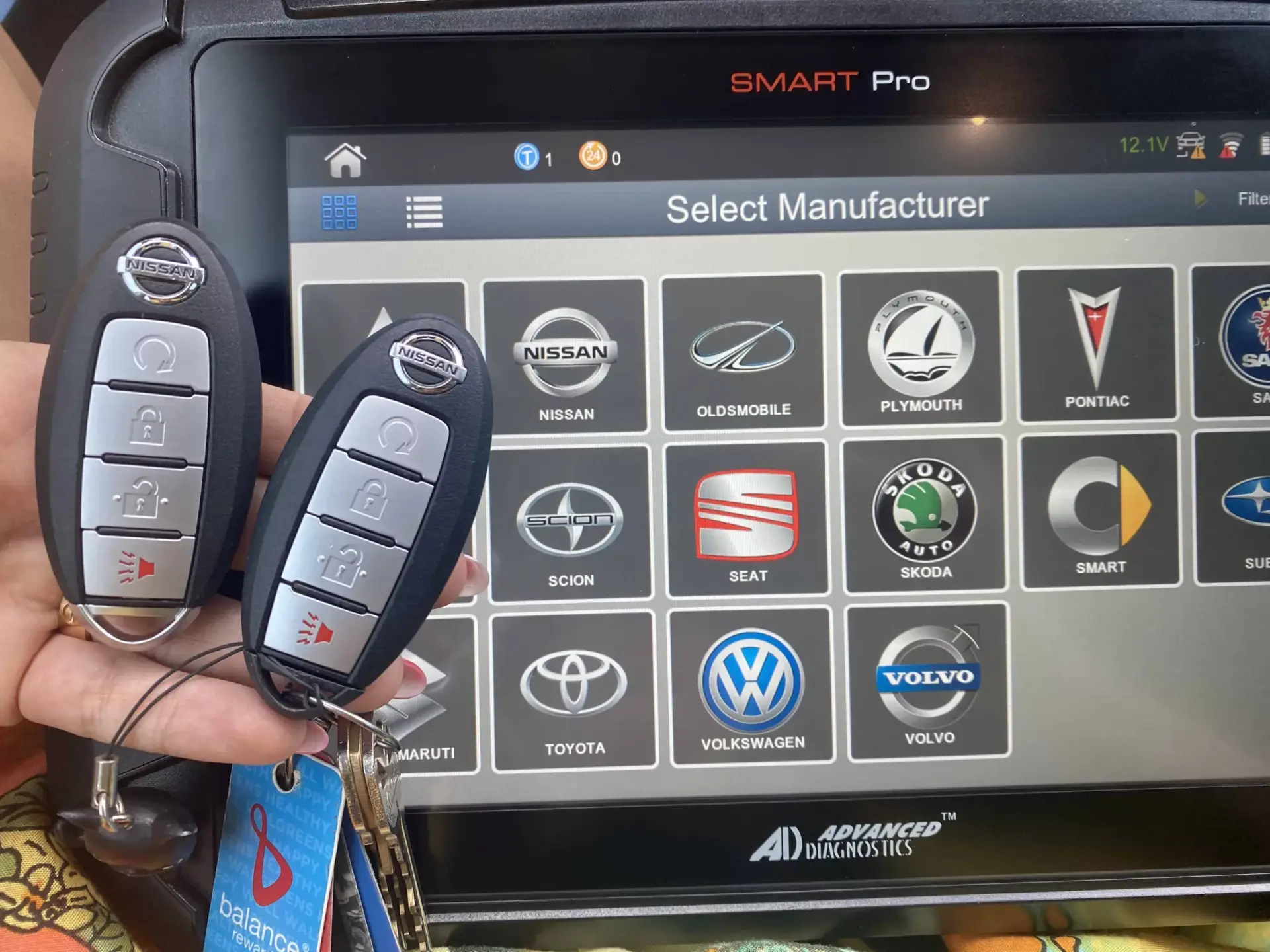Nissan Murano Key Fob Replacement A hand holds a Nissan smart key fob in front of an OTOFIX Smart Pro key programming device displaying a manufacturer selection screen.