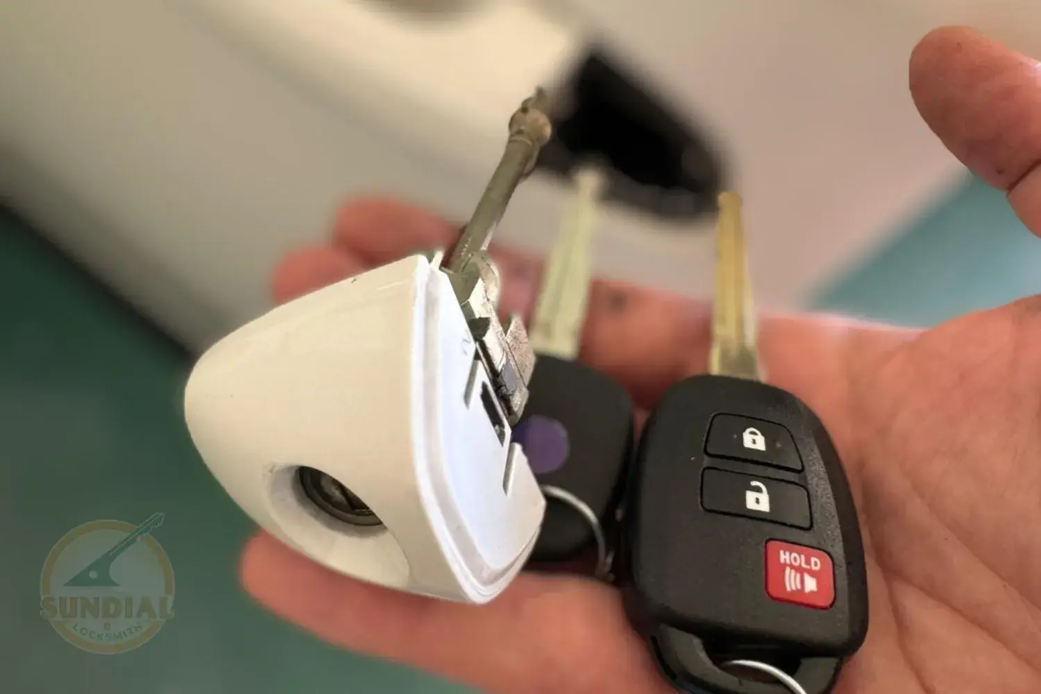 Can a Locksmith Make a Key from a Lock? Unveiling the Art Behind Key Creation A hand holding a Toyota car key fob alongside a small white device used for key cutting or programming.
