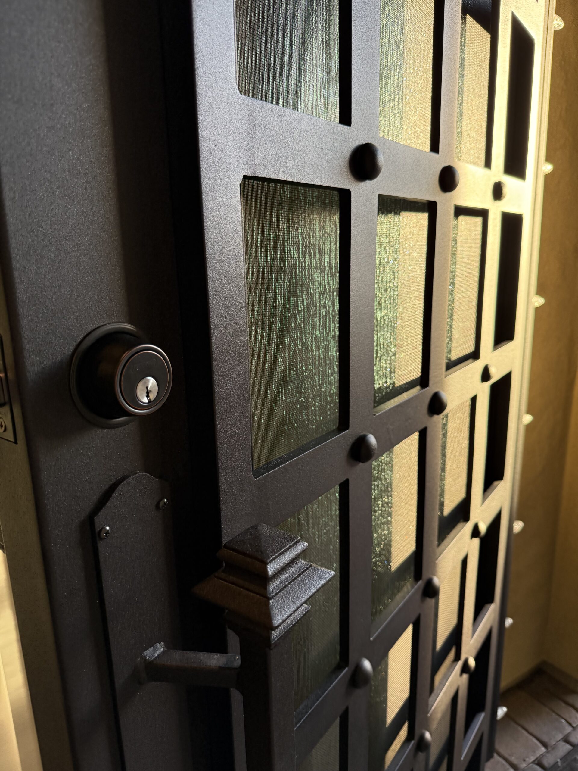 5 Essential Tips to Keep Your Home Secure A heavy black metal security door with decorative grid panels, frosted glass inserts, and a brass deadbolt lock installed on the interior side.