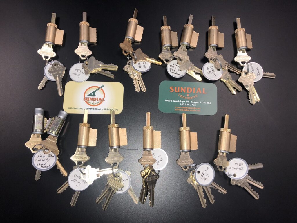 Can a Locksmith Rekey a Lock to Match a Key You Already Use? A large collection of brass lock cylinders each paired with their corresponding keys, displayed alongside Sundial Locksmith business cards and a branded tin.