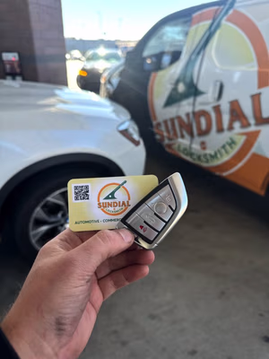 How to Get a Locksmith Quote That Won't Change When the Tech Shows Up A hand holds a modern car key fob alongside a Sundial Locksmith business card in front of a branded Sundial Locksmith service van.