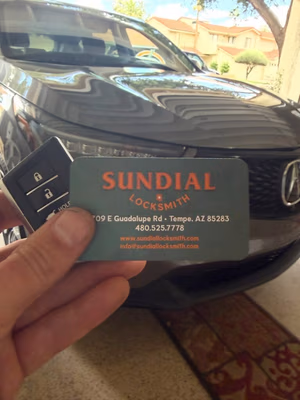 Why a Locksmith with a Real Storefront Is Different from a Van with a Phone Number A hand holding a Sundial Locksmith business card and a car key fob in front of a dark-colored Acura vehicle.