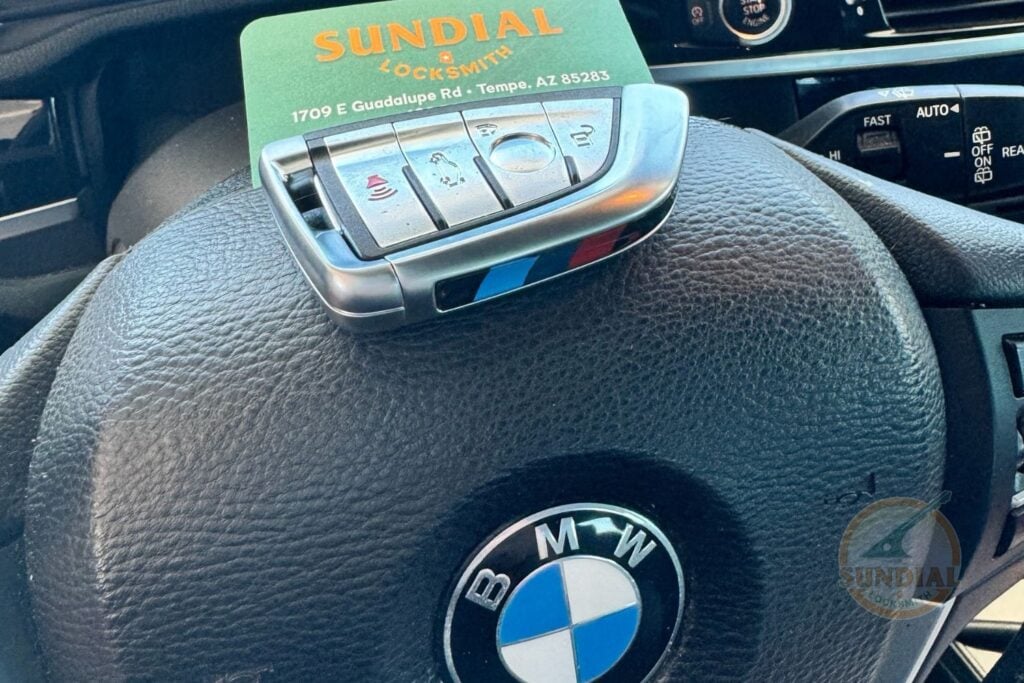 Why a Locksmith with a Real Storefront Is Different from a Van with a Phone Number A BMW smart key fob resting on a BMW steering wheel with a Sundial Locksmith business card placed on top.