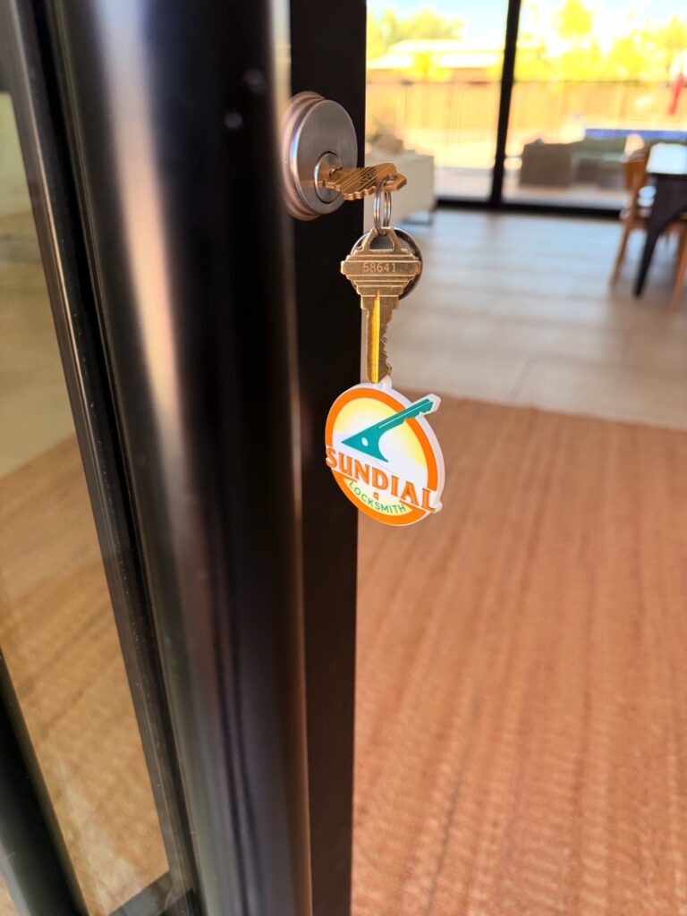 How a Locksmith Can Walk Through Your Home and Tell You What's Weak A brass key with an orange Sundial Locksmith branded keychain tag inserted into a residential door lock, with a bright living space visible in the background.