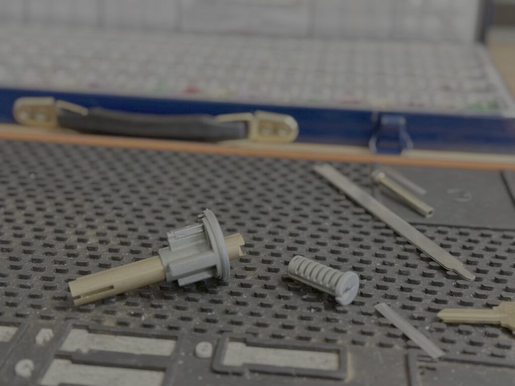 Can You Rekey Your Own Locks? What DIY Gets Right and Wrong Disassembled lock cylinder parts including a plug, pins, and small tools laid out on a textured gray work mat.