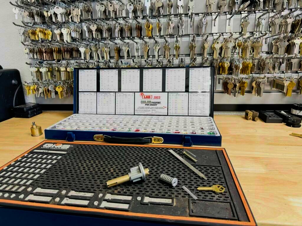 Can You Rekey Your Own Locks? What DIY Gets Right and Wrong A locksmith workbench with a blue key blank organizer case, lock cylinder tools, and brass keys in front of a wall display filled with hundreds of key blanks.