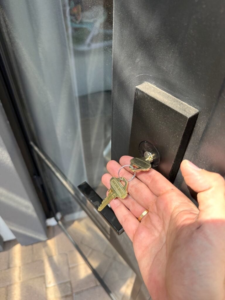 Rekeying a Commercial Building: What's Involved When You Have Dozens of Locks A person holds a set of brass keys in their open palm next to a black door handle and lock on a modern entry door.