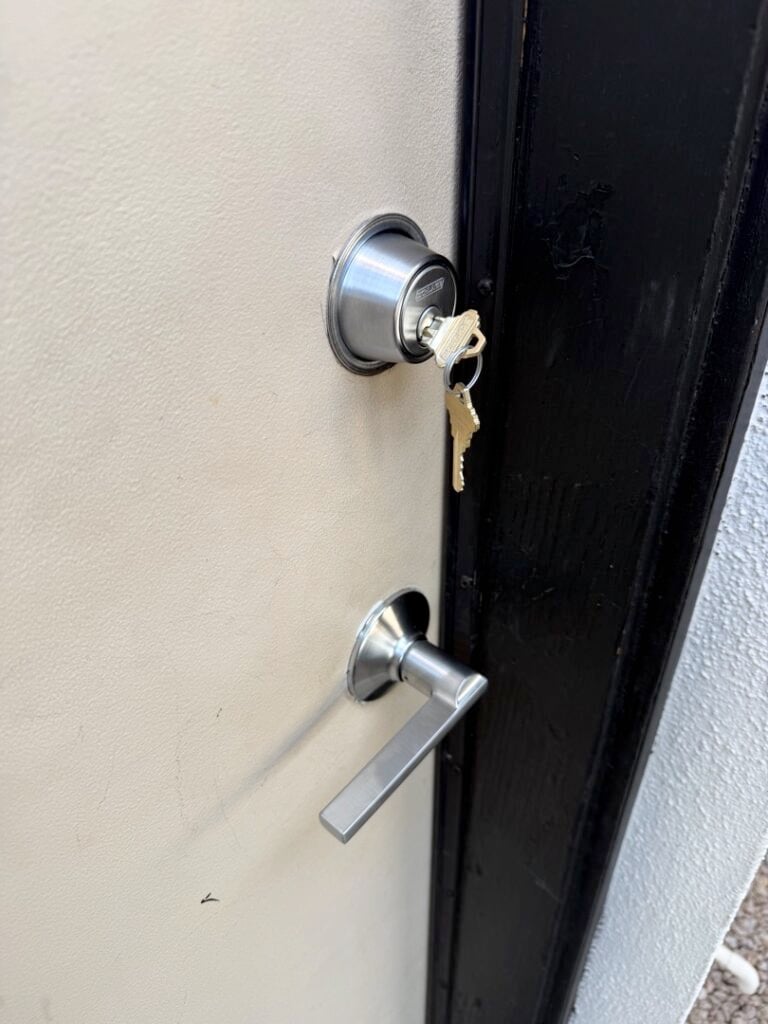 Same-Day Deadbolt Replacement: When to Skip the Hardware Store Trip A black exterior door featuring a silver deadbolt lock with keys inserted and a lever-style door handle below it.