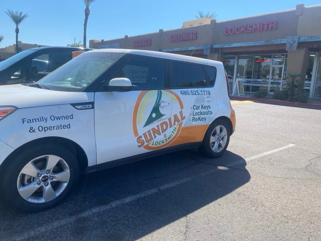 Sundial Locksmith Branded Service Vehicle A white Kia Soul wrapped with Sundial Locksmith branding, including the company logo, phone number, and 'Family Owned & Operated' text, parked in a sunny strip mall parking lot.