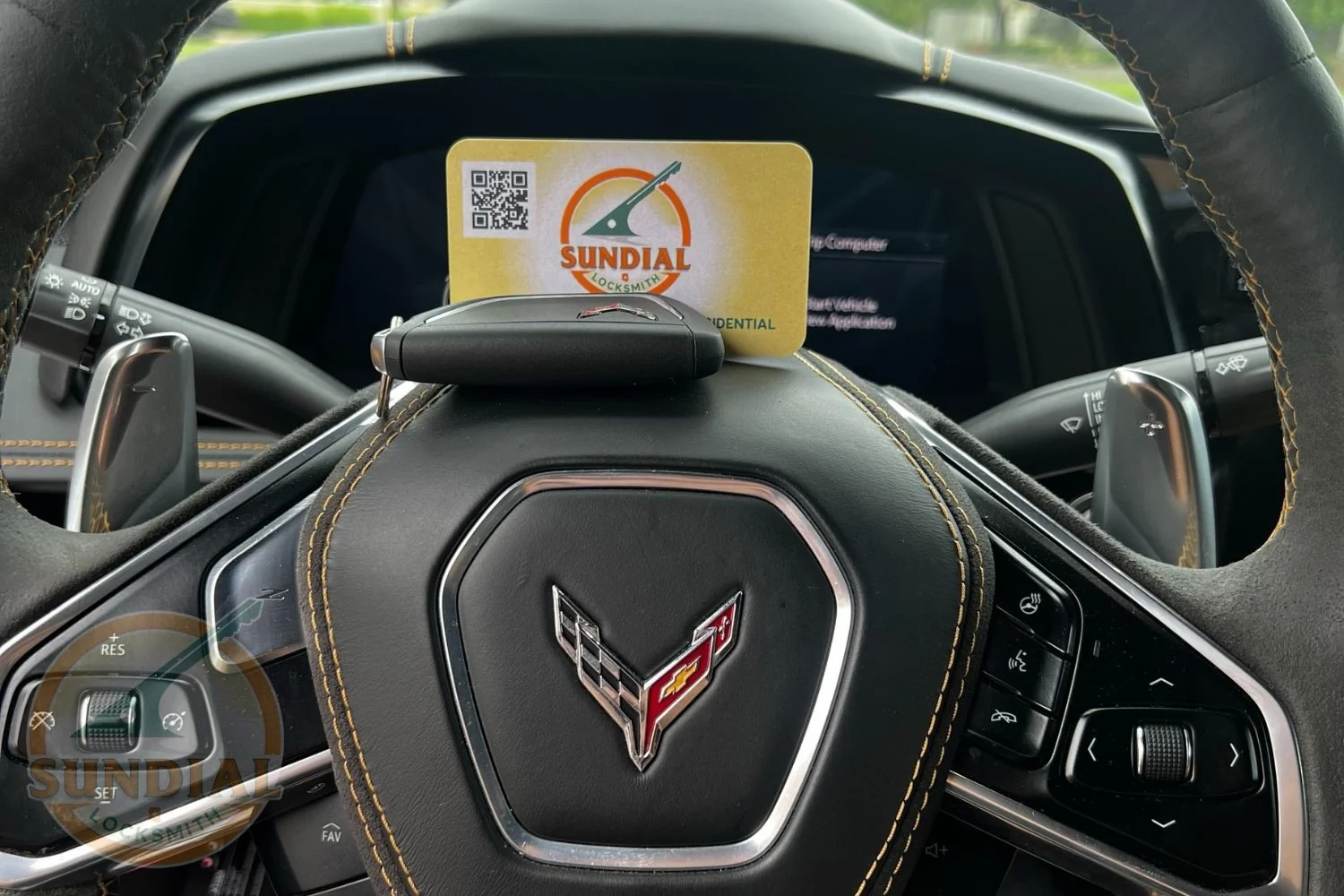 How to Get the Key Code for Your Car — and What a Locksmith Does with It A Sundial Locksmith business card with QR code displayed on the steering wheel of a Chevrolet Corvette with a visible crossed-flags emblem.