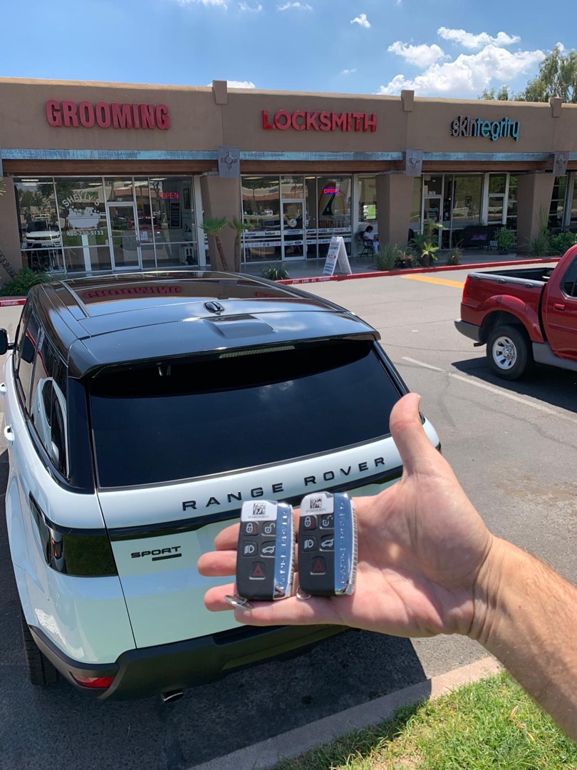 Key Fob Not Reaching as Far as It Used To? Here's Why A hand holding two Range Rover key fobs in a parking lot in front of a strip mall with a white Range Rover Evoque parked nearby.