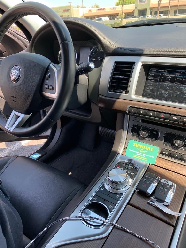 Access Control for an Office Suite: What to Expect from Installation Close-up view of a Jaguar car interior showing the steering wheel, center console, gear shift, and infotainment system with a green locksmith service tag visible on the seat.