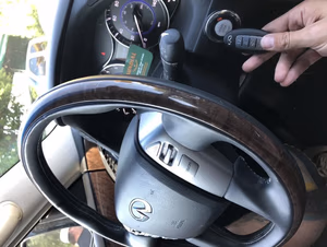 Stuck Key in the Ignition: What to Do Before You Force It A hand holding a black key fob next to the steering wheel and ignition of a Lexus vehicle during a locksmith programming service.