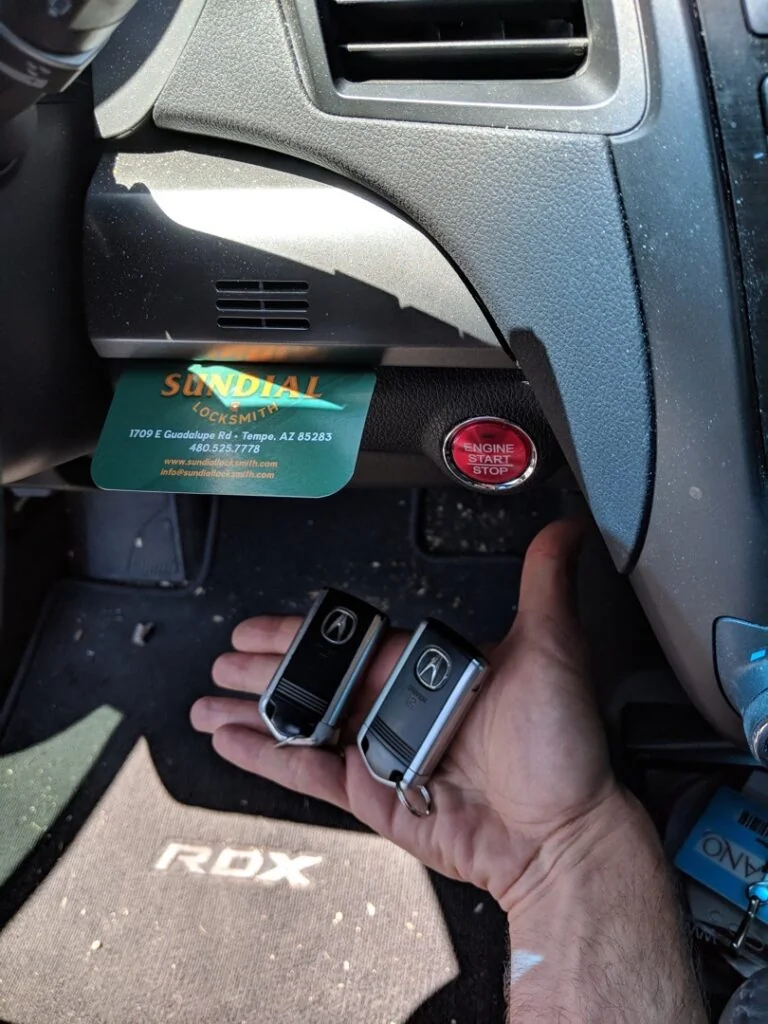 Stuck Key in the Ignition: What to Do Before You Force It A locksmith holds a new Acura key fob next to the push-button ignition of an Acura RDX dashboard, with a Sundial Locksmith business card visible in the background.