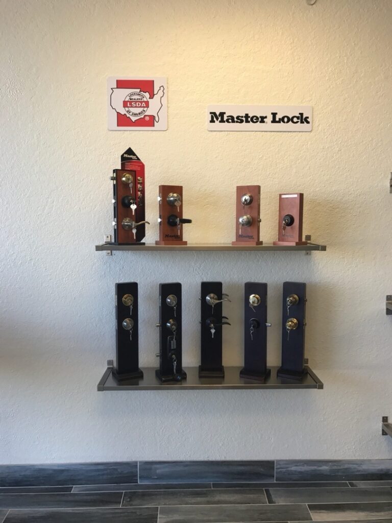 How to Make Your Front Door Frame More Resistant to Forced Entry Two wall-mounted metal shelves displaying a variety of Master Lock door locks and deadbolts in a locksmith showroom.