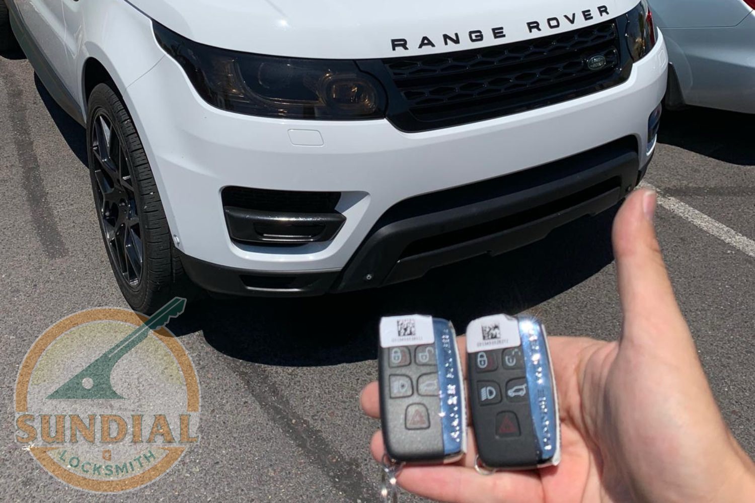 Key Fob Not Reaching as Far as It Used To? Here's Why A hand holding two Range Rover smart key fobs in front of a white Range Rover Sport SUV in a parking lot.