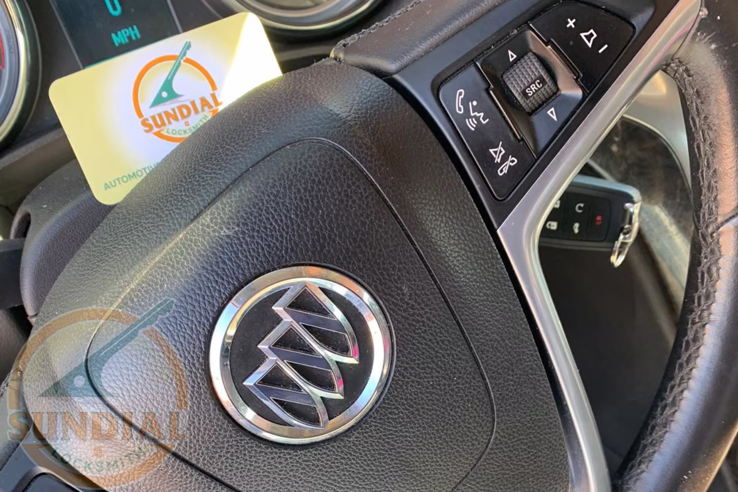 Ignition Replacement: How Much It Costs and How Long It Takes Close-up of a Buick steering wheel with a Sundial Locksmith business card tucked into the dashboard, showing steering column controls.