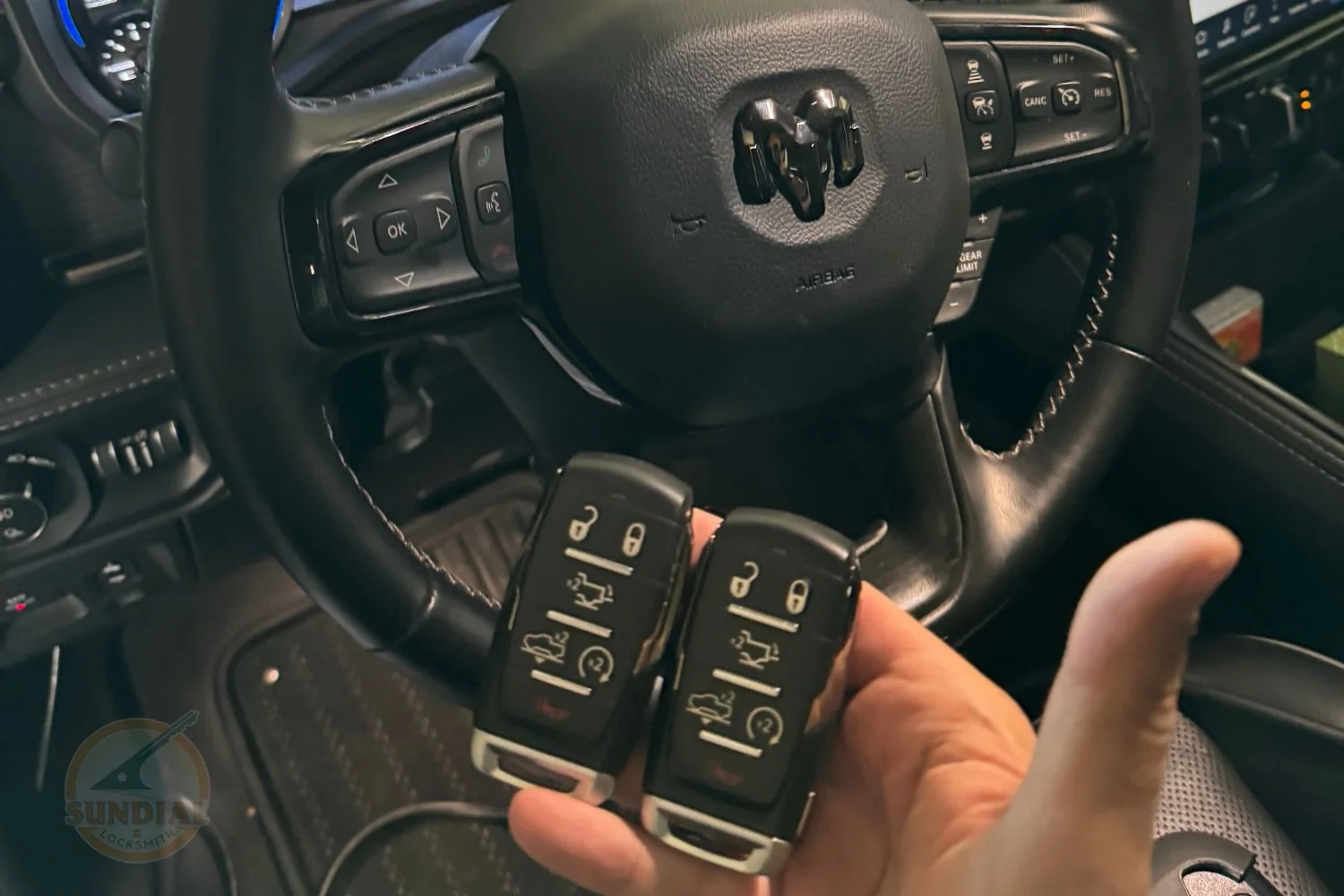 How Long Does 'All Keys Lost' Programming Actually Take? A hand holding two Ram truck smart key fobs in front of a Ram vehicle's steering wheel and dashboard interior.