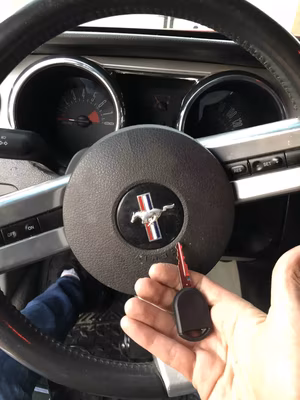 Car key Replacement – The Solution for All Your Car Key Troubles A locksmith holds a Ford Mustang key fob inside a Mustang vehicle with the steering wheel and dashboard visible in the background.