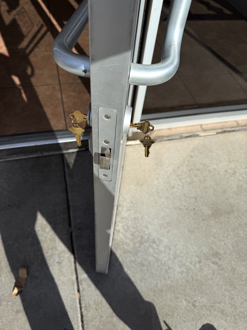 How to Secure a Sliding Glass Door That a Burglar Can't Just Lift Off A close-up view of a sliding screen door's latch mechanism with two keys inserted into separate locks on an aluminum door frame.