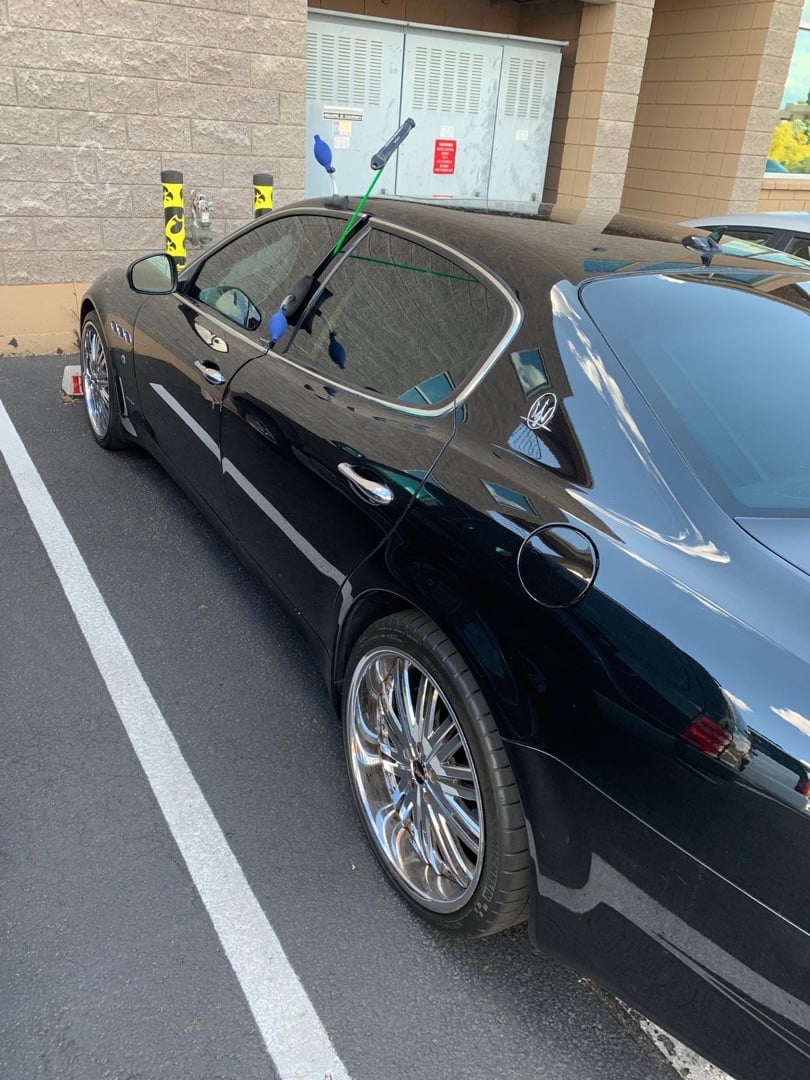 What a Slim Jim Is — and Why a Pro Rarely Needs One Anymore A shiny black luxury sedan parked in a parking lot with yellow locksmith slim jim tools visible near the door and window.