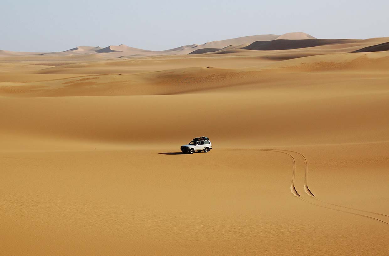 A vehicle drives through the desert, with sand dunes and the Pyramids of Giza visible in the background.