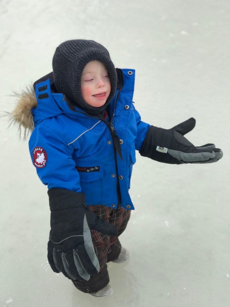 Child in warm blue winter coat, black hat, and gloves playing in snow.