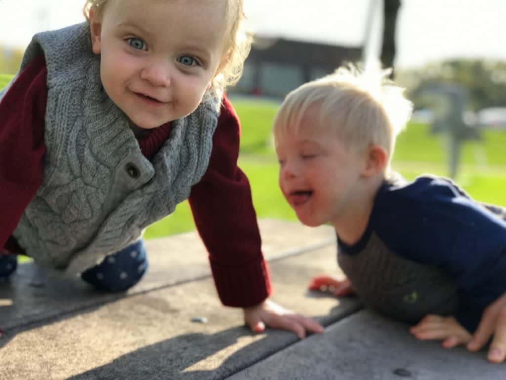 Alt text: Two young children playing outdoors, one smiling, the other crying, on a sunny day.