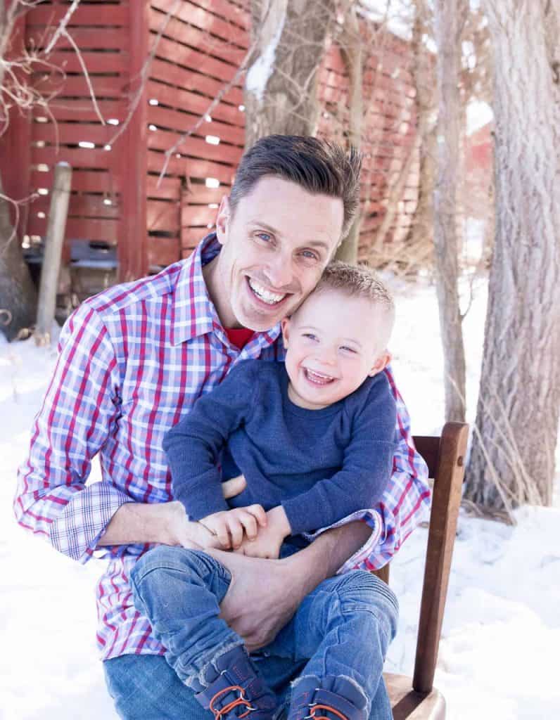 Happy Dad and Kid in Winter Outdoors. Alt text: Smiling father and son enjoying winter outdoors, surrounded by snow and trees.
