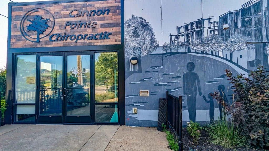 Modern chiropractic clinic entrance with artistic mural and natural landscaping for health and wellness.