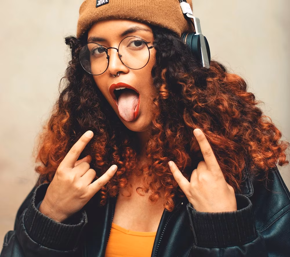 jeune femme aux cheveux bouclés tirant la langue et faisant des signes rock n' roll avec ses mains