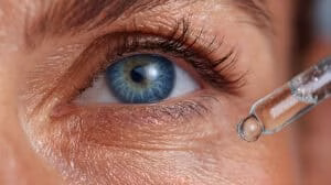 Close up view of a pipette delivering eye drops to a woman's vibrant blue eye, enhancing eye health and promoting clear vision with a soothing moisturizing serum