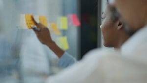 News 31 Business people placing reminder post-it notes on board during conference, illustrating how to send sales event reminders.