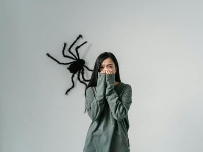 Woman covering her mouth, large black spider decoration on the wall behind her