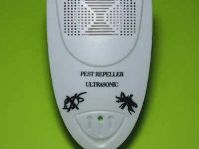 White ultrasonic pest repeller with 'PEST REPELLER ULTRASONIC' text and insect icons on a green background