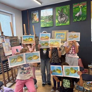 kurs_rysunku_dla_Dzieci_Sealart_szkoła_rysunku_warszawa-legionowo | Sealart szkoła rysunku Group of children in art class holding up lemon-themed drawings in a bright studio with easels and painted animal pictures on the dark wall behind them.